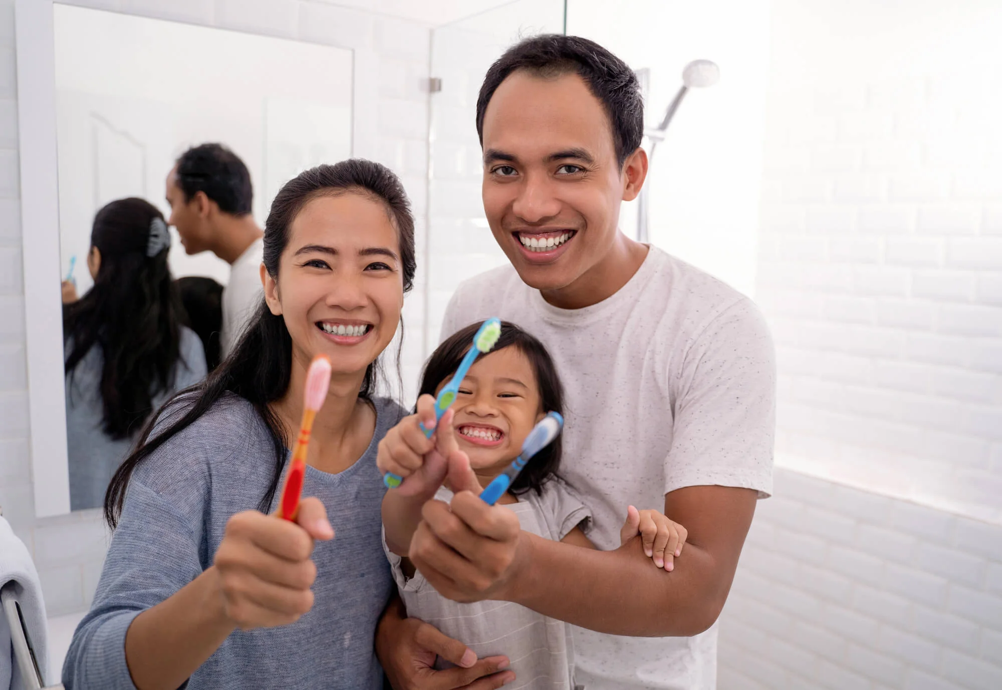 Family holding toothbrushes and smiling in bathroom Routine dental care New Jersey (1)